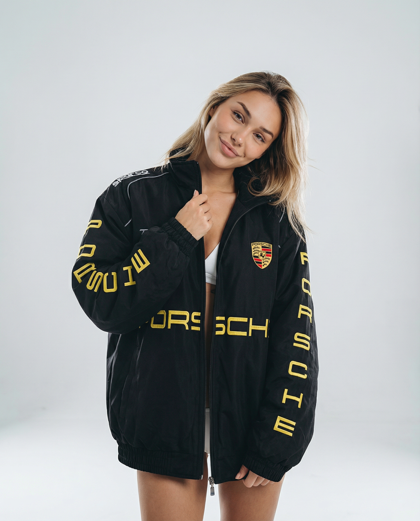 Woman wearing a black Porsche jacket with yellow text on a white background