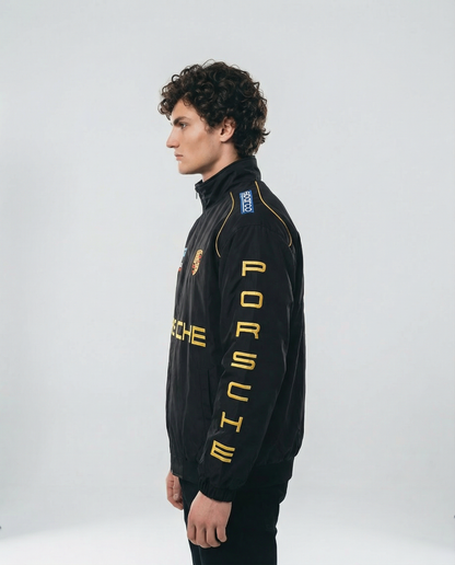 Person wearing a black Porsche jacket with yellow text on a white background - Side profile of Porsche Racing Jacket highlighting sleeve detailing and modern streetwear silhouette
