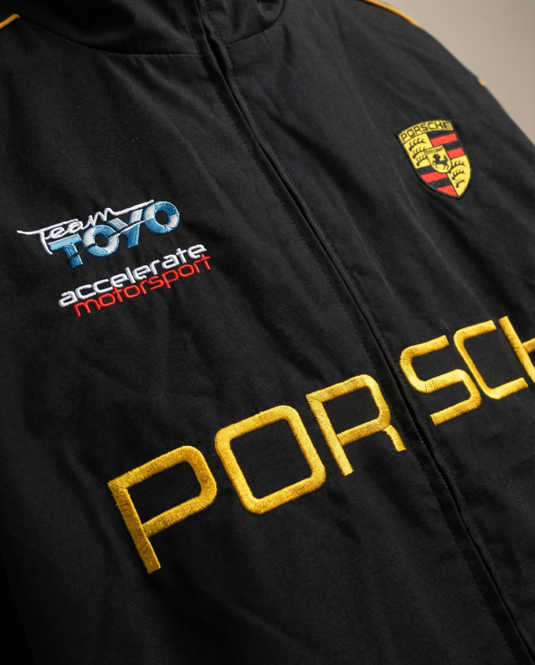 Black jacket with Porsche logo and branding on a neutral background. Close-up of Porsche Racing Jacket logo with detailed embroidery and premium stitching
