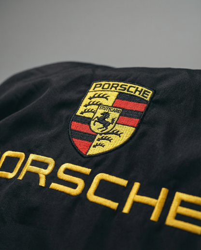 Close-up of a Porsche logo and text on a black background. Close-up of Porsche Racing Jacket logo with detailed embroidery and premium stitching
