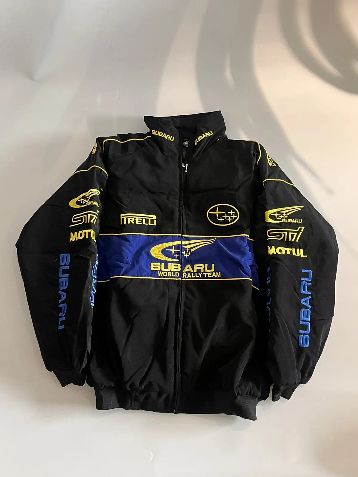Subaru World Rally Team Vintage Racing Jacket – black with yellow and blue detailing, retro motorsport style shown front and back.