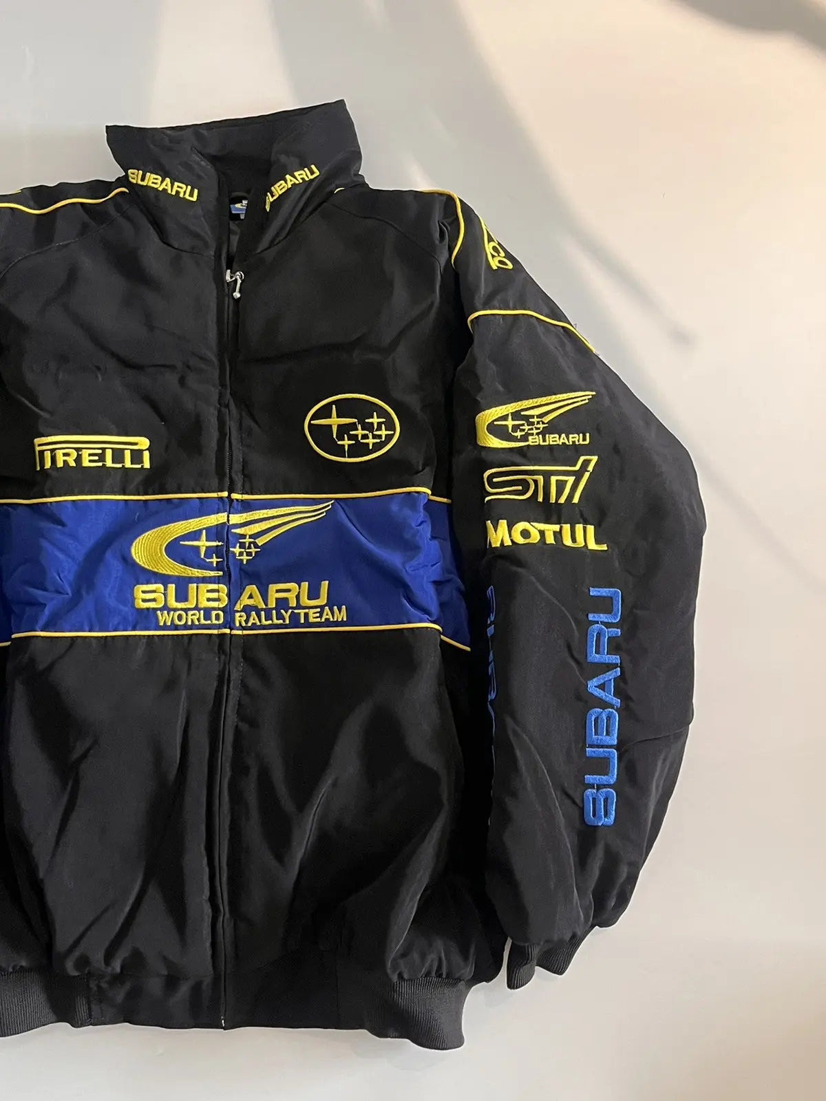 Subaru World Rally Team Vintage Racing Jacket – black with yellow and blue detailing, retro motorsport style shown front and back.