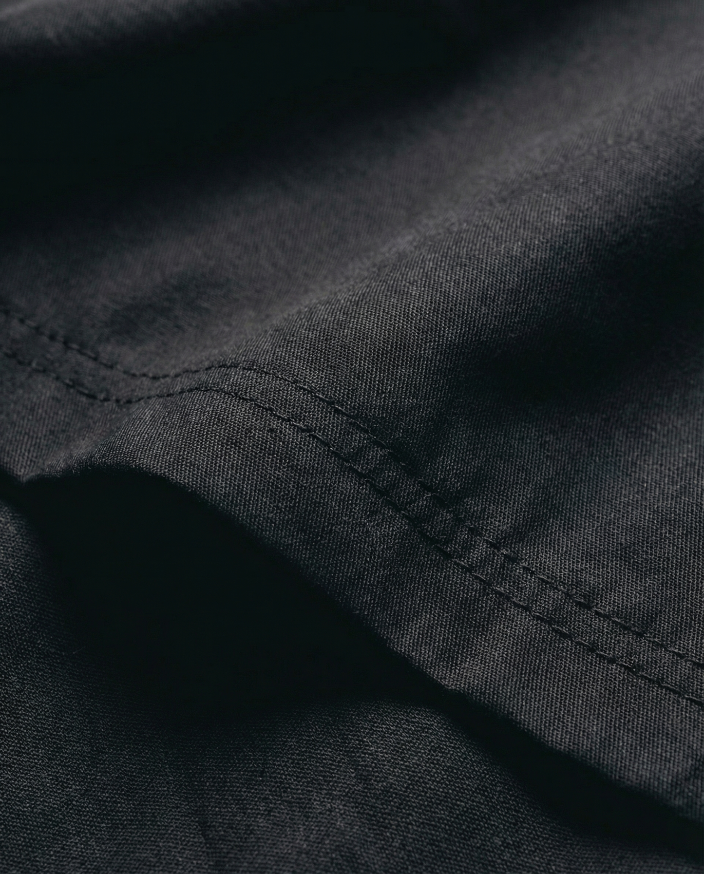 Close-up of black fabric with visible stitching. Fabric texture detail of Porsche Racing Jacket showing durable material and quality construction
